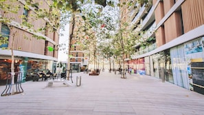 A pedestrian walkway lined with trees and buildings, featuring outdoor seating areas and a central bench.