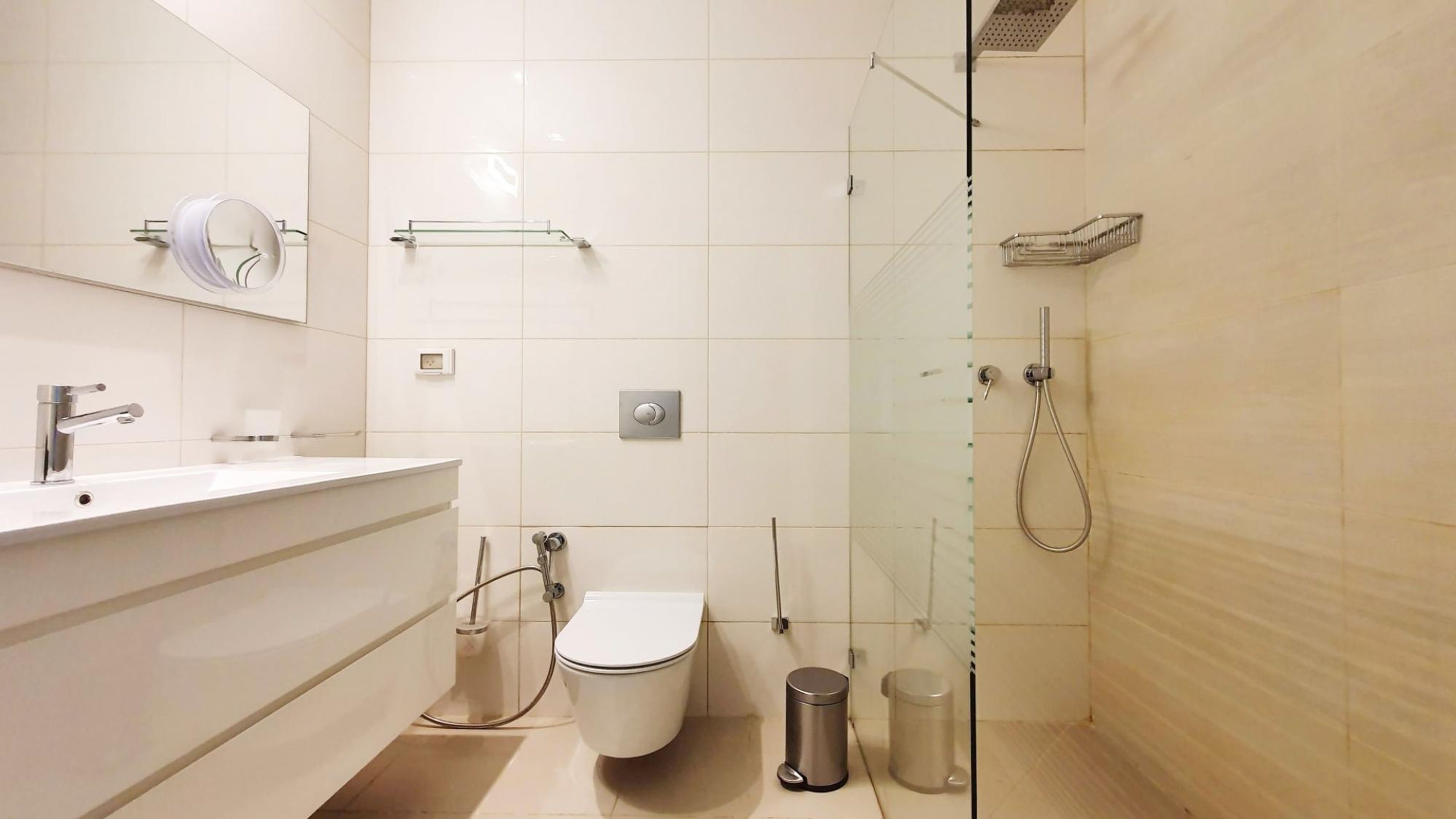 Ein modernes Badezimmer mit einer Duschkabine, Toilette, Waschbecken mit Spiegel und einem Mülleimer.