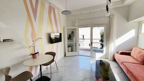 A modern living room with a sofa, a dining table with chairs, a TV mounted on the wall, and a sliding glass door leading to an outdoor balcony. - Yosef Terracotta in Tel Aviv-yafo (Tel Aviv)