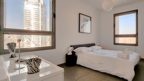 A modern bedroom with a bed, a desk with a lamp, and a window with a city view.