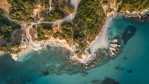 Vista aérea de una zona costera con playa de arena, costa rocosa y abundante vegetación.