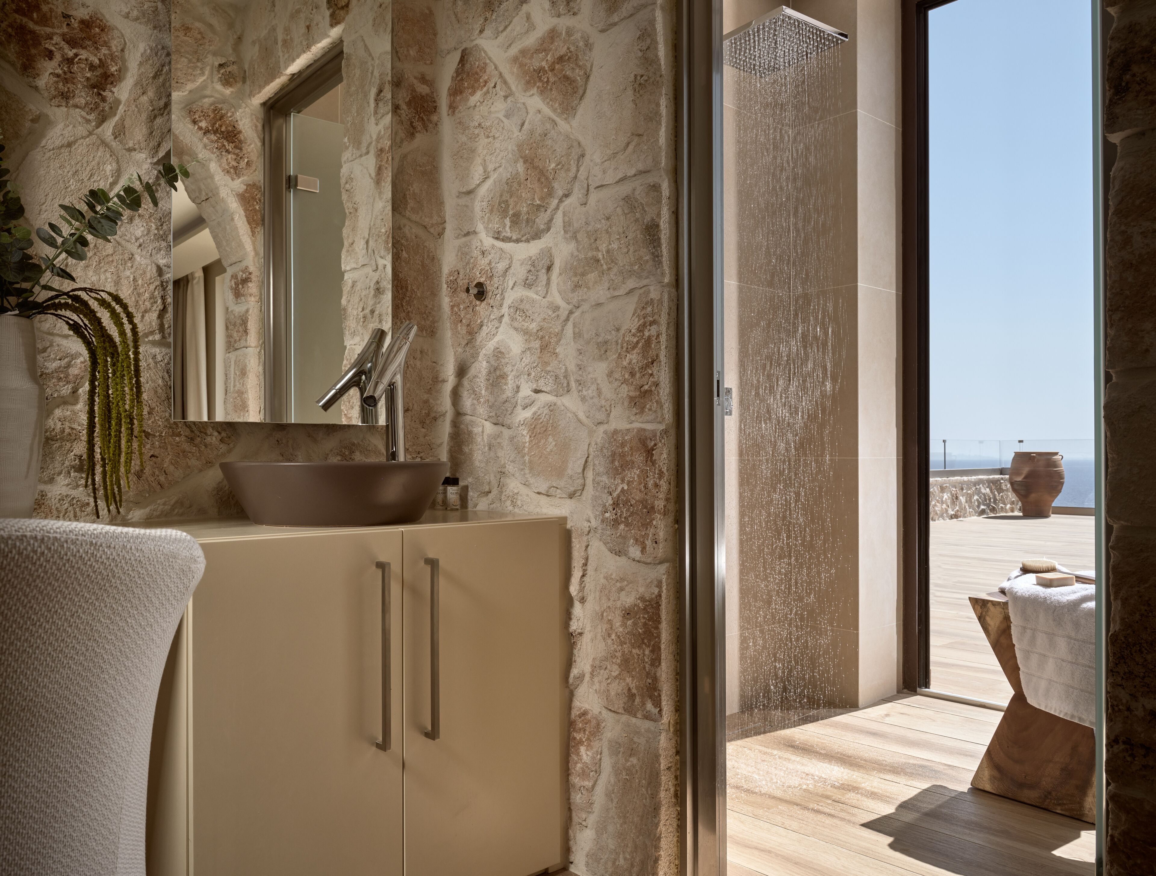 Un ba ño con pared de piedra, lavabo, espejo y ducha.
