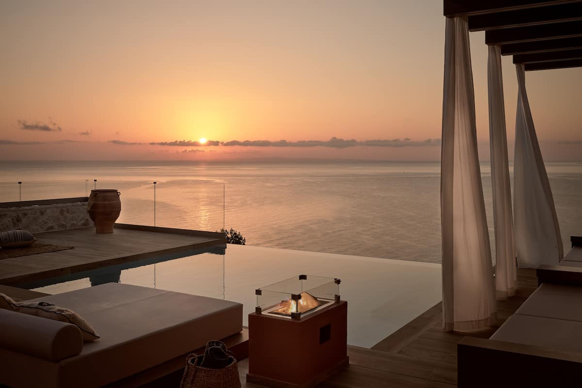 A sunset view from a balcony with a pool, lounge chairs, and a table with a candle.