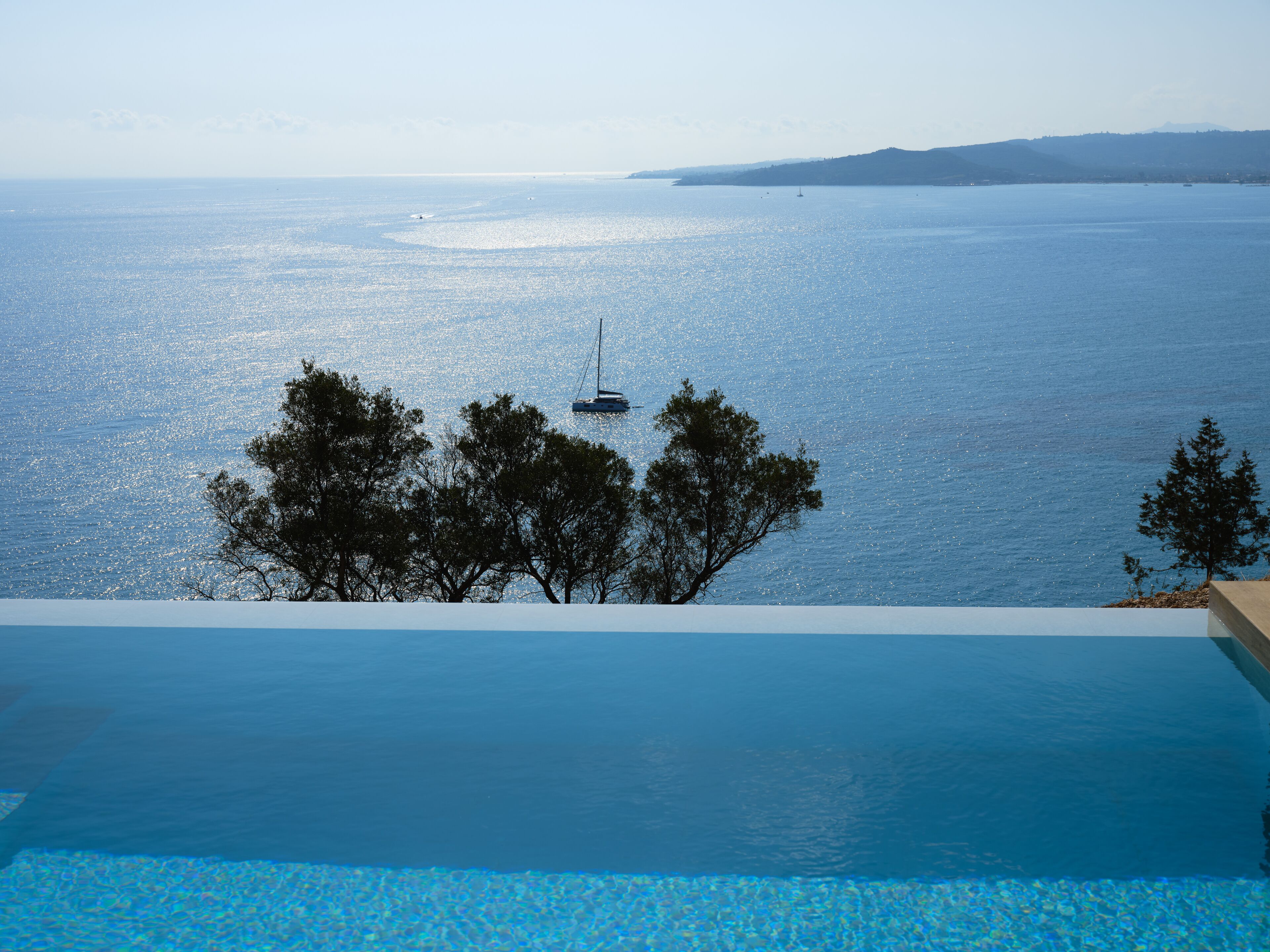 Una piscina con vista al mar y un velero a lo lejos.