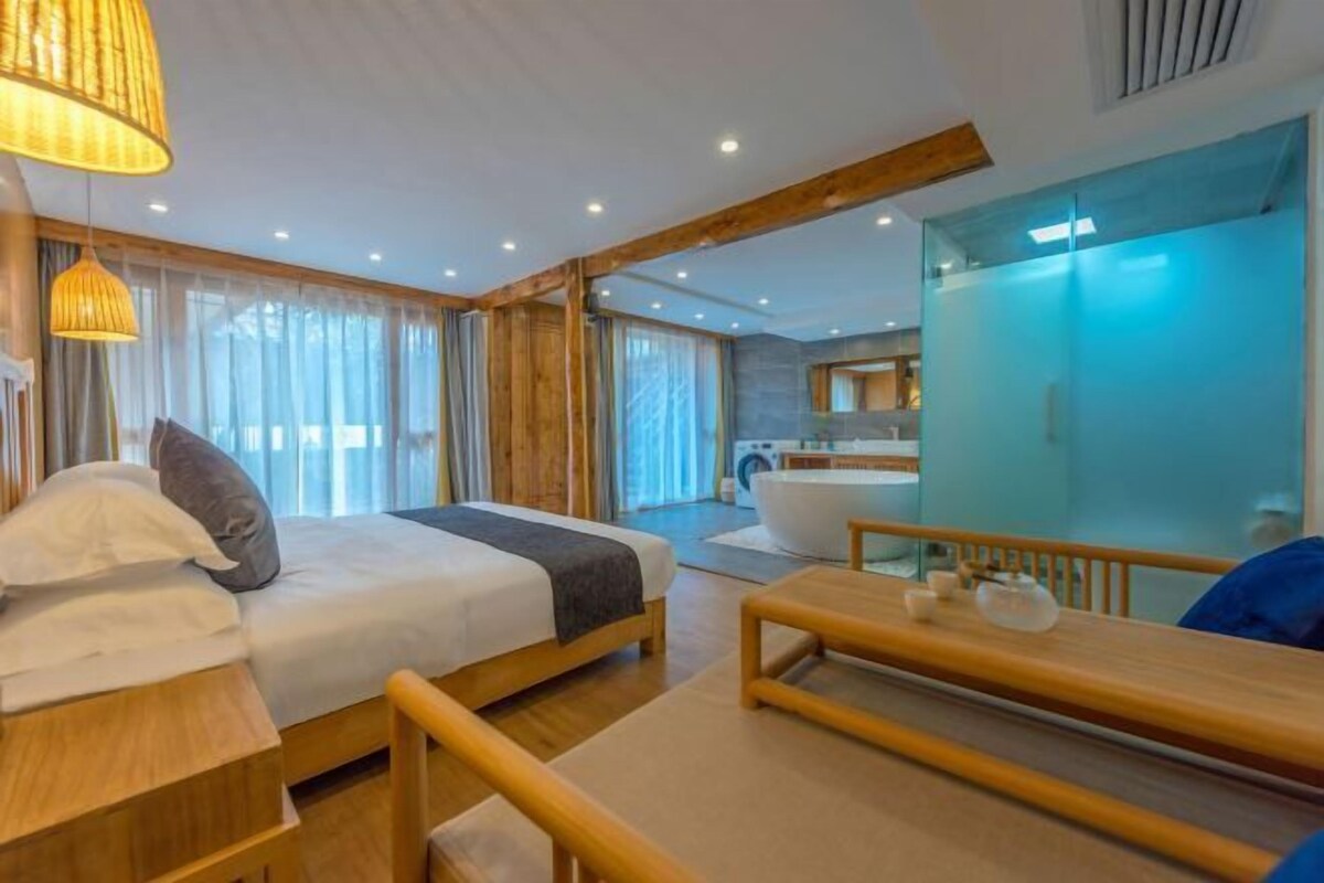 Ein modernes Hotelzimmer mit Bett, Nachttisch und einem großen Fenster mit Vorhängen.