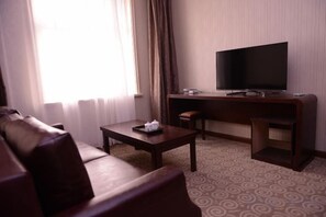 Habitación de hotel con sofá de cuero, mesa de centro de madera, televisor de pantalla plana y escritorio.
