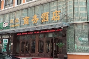 Un hôtel avec une façade en verre, une enseigne avec des caractères chinois et un auvent rouge.
