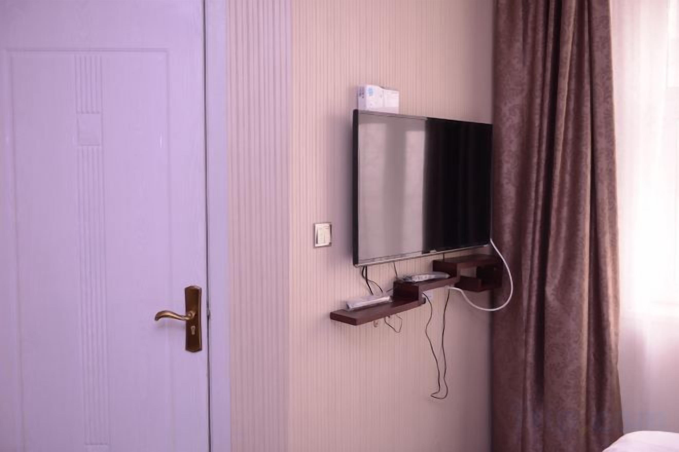 Una habitación con una puerta cerrada, un televisor montado y una cortina.