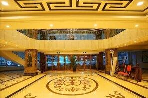 Een hotel lobby met een monumentale trap, een decoratief vloerpatroon in het midden en een zithoek met stoelen.