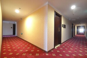 A hotel corridor with carpeted flooring, a wooden door, and a light fixture on the ceiling.