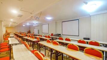A conference room with multiple tables and chairs, a projector screen, and a whiteboard.