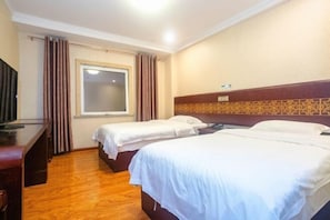 Habitación de hotel con dos camas, un escritorio, televisor y ventana con cortinas.