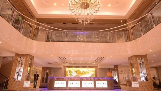 A hotel lobby with a grand chandelier, a reception desk, and a person standing near the entrance.