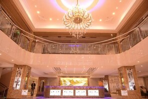 Een hotel lobby met een weelderige kroonluchter, een receptiebalie en een persoon nabij de ingang.