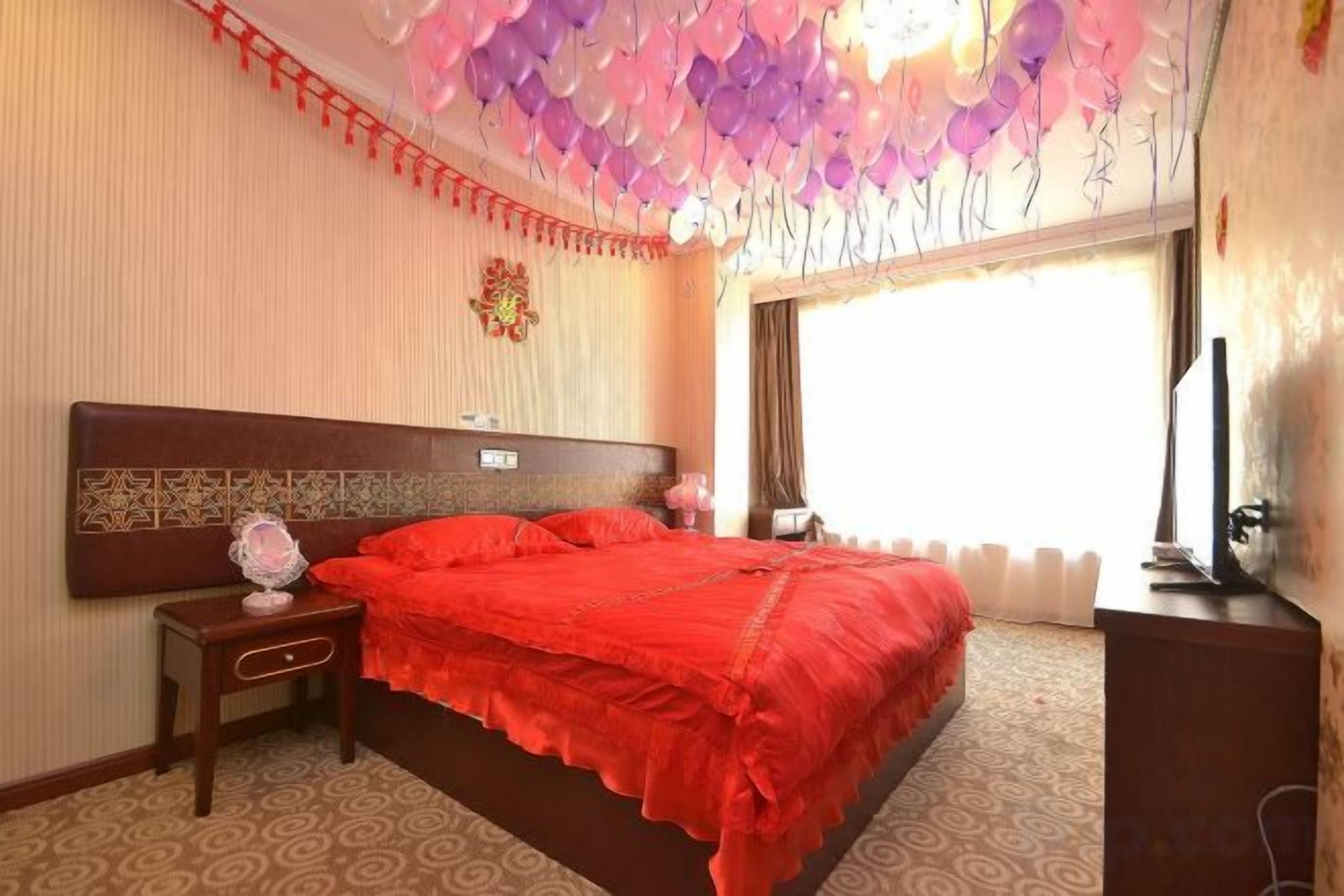 Una habitación de hotel con una cama grande, una mesita de noche, un televisor y una ventana con cortinas.