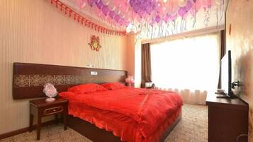 Una habitación de hotel con una cama grande, una mesita de noche, un televisor y una ventana con cortinas.