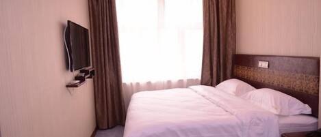Habitación de hotel con cama, televisor en la pared y ventana con cortinas.