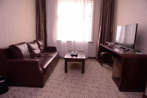 Ein Hotelzimmer mit einer Couch, einem kleinen Tisch, einem Fernseher und einem Schreibtisch.