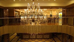 A grand lobby with a large, ornate chandelier, marble flooring, and a glass railing.