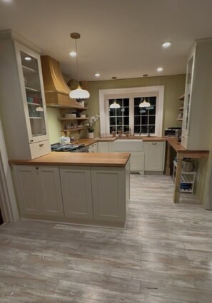 A kitchen with a central island, wooden countertops, and pendant lighting.