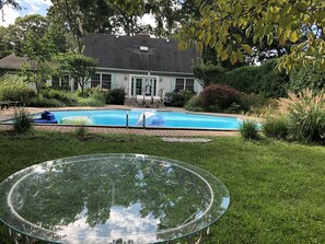 A backyard with a swimming pool, a glass table, and a house in the background.