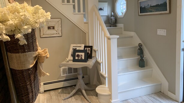 Una escalera con barandillas blancas y una pared blanca con un cuadro enmarcado y un jarrón de flores.
