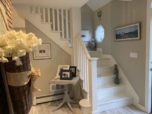 A staircase with white railings and a white wall with a framed picture and a vase of flowers. - Beach house cape in North Fork's wine country (Mattituck)