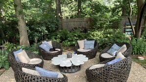 Un espacio de descanso en un jardín con mobiliario de mimbre y una mesa central.