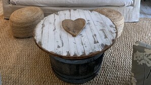 Una sala de estar acogedora con un sofá de color claro, una mesita de centro redonda con forma de corazón y una silla de madera rústica.