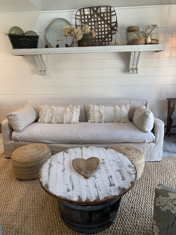 A cozy living room with a light-colored sofa, a round coffee table with a heart-shaped top, and a rustic wooden chair.