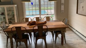 Un comedor con una mesa de madera, seis sillas, dos lámparas colgantes y vistas a un patio trasero a través de un ventanal.