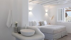 Ein modernes Schlafzimmer mit einem großen Bett, einem runden weißen Waschbecken und einem Fenster mit Blick nach draußen.