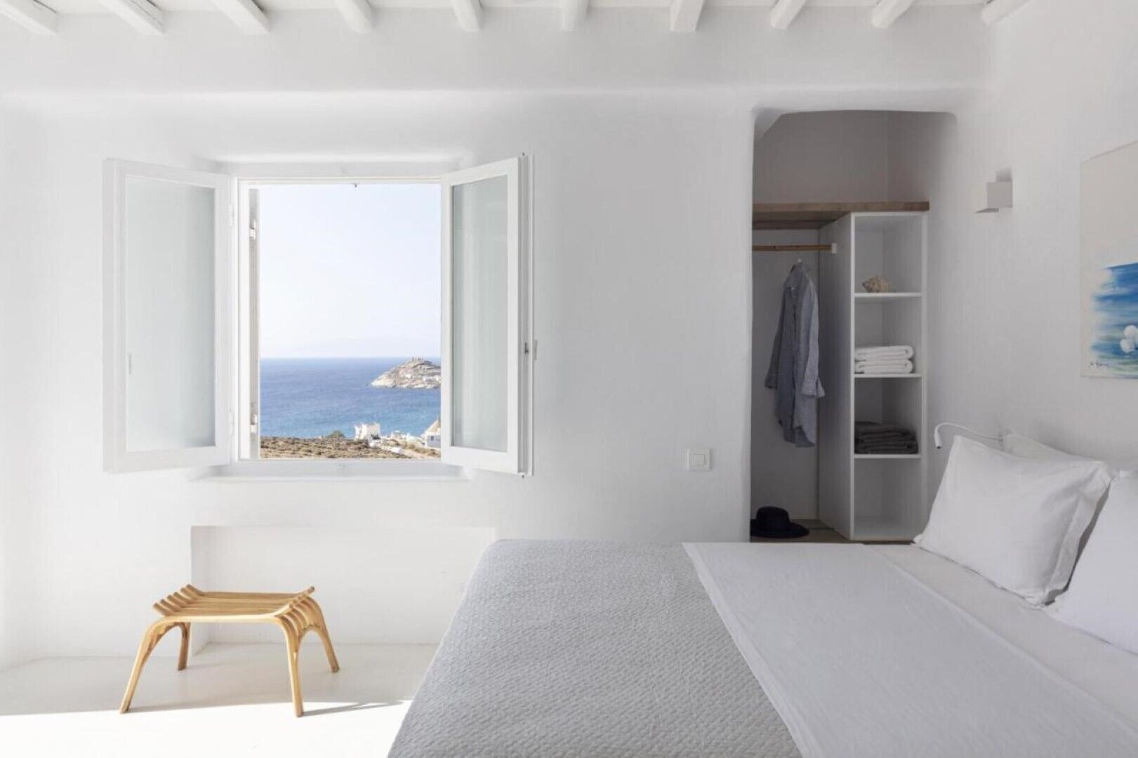 Un dormitori minimalista amb un gran finestral que ofereix vistes al mar, una panxa de fusta i un armari ben organitzat.