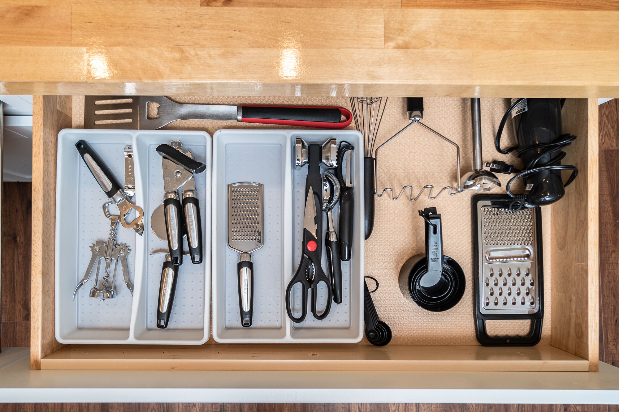 A drawer with various kitchen utensils organized in compartments.