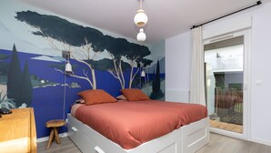 Un dormitorio con una cama, un taburete de madera, una mesita de noche y un mural en la pared.