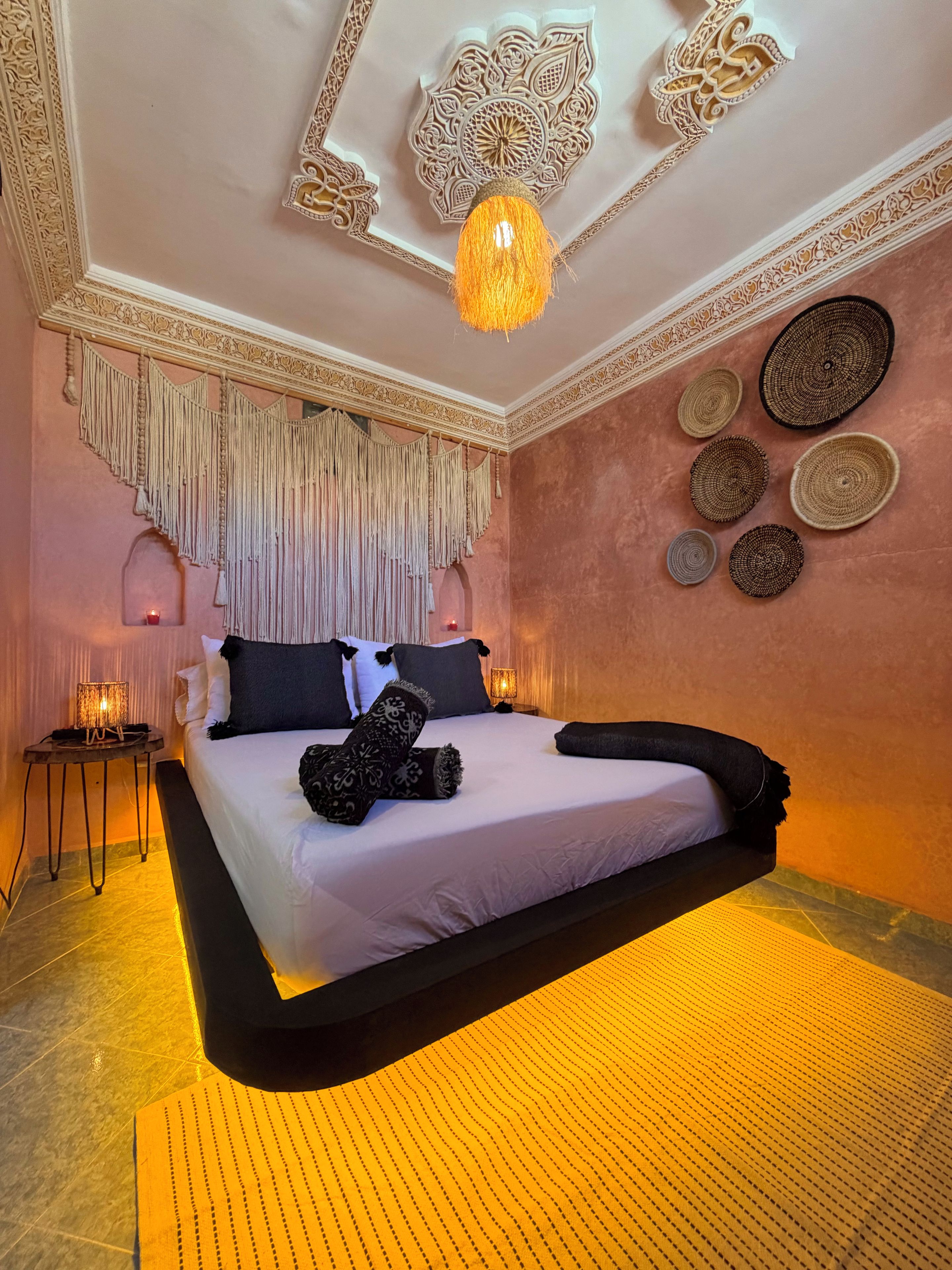 Een slaapkamer met een bed, decoratieve wandversieringen, een hanglamp en een klein tafeltje met een lamp.