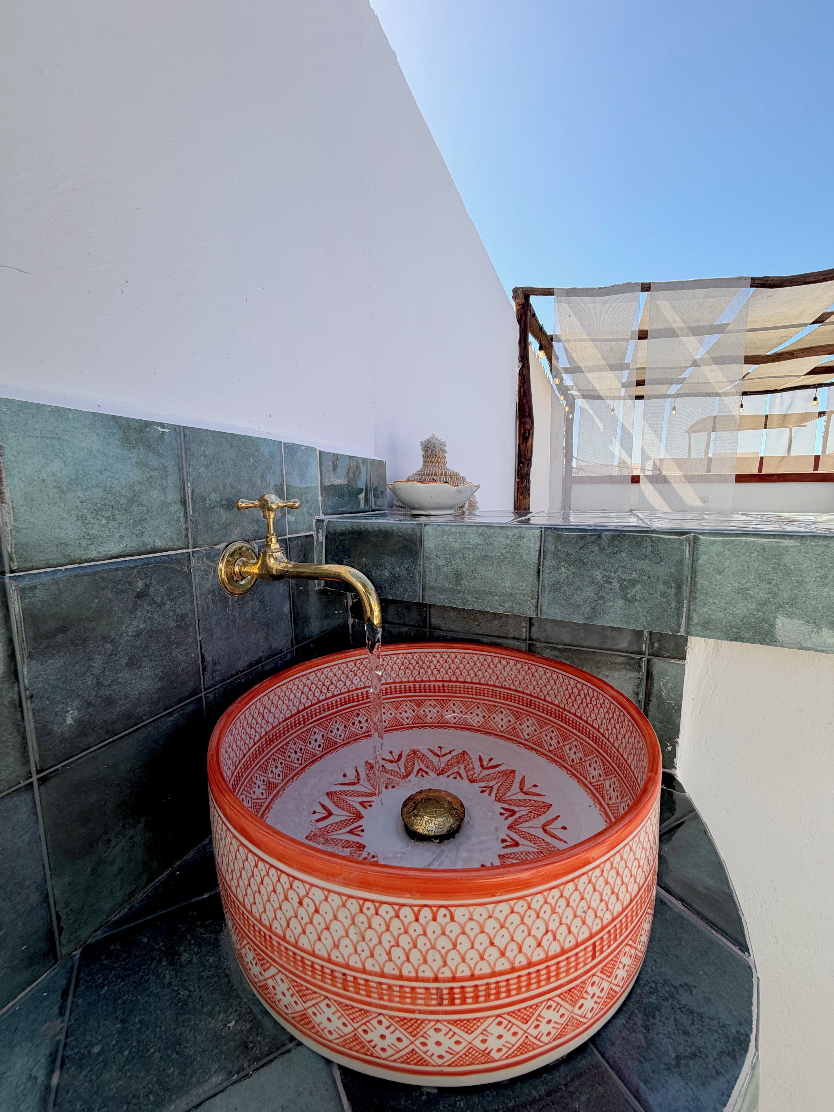 Uma pia redonda e decorada com uma torneira dourada, em frente a uma parede com azulejos e padrão geométrico.
