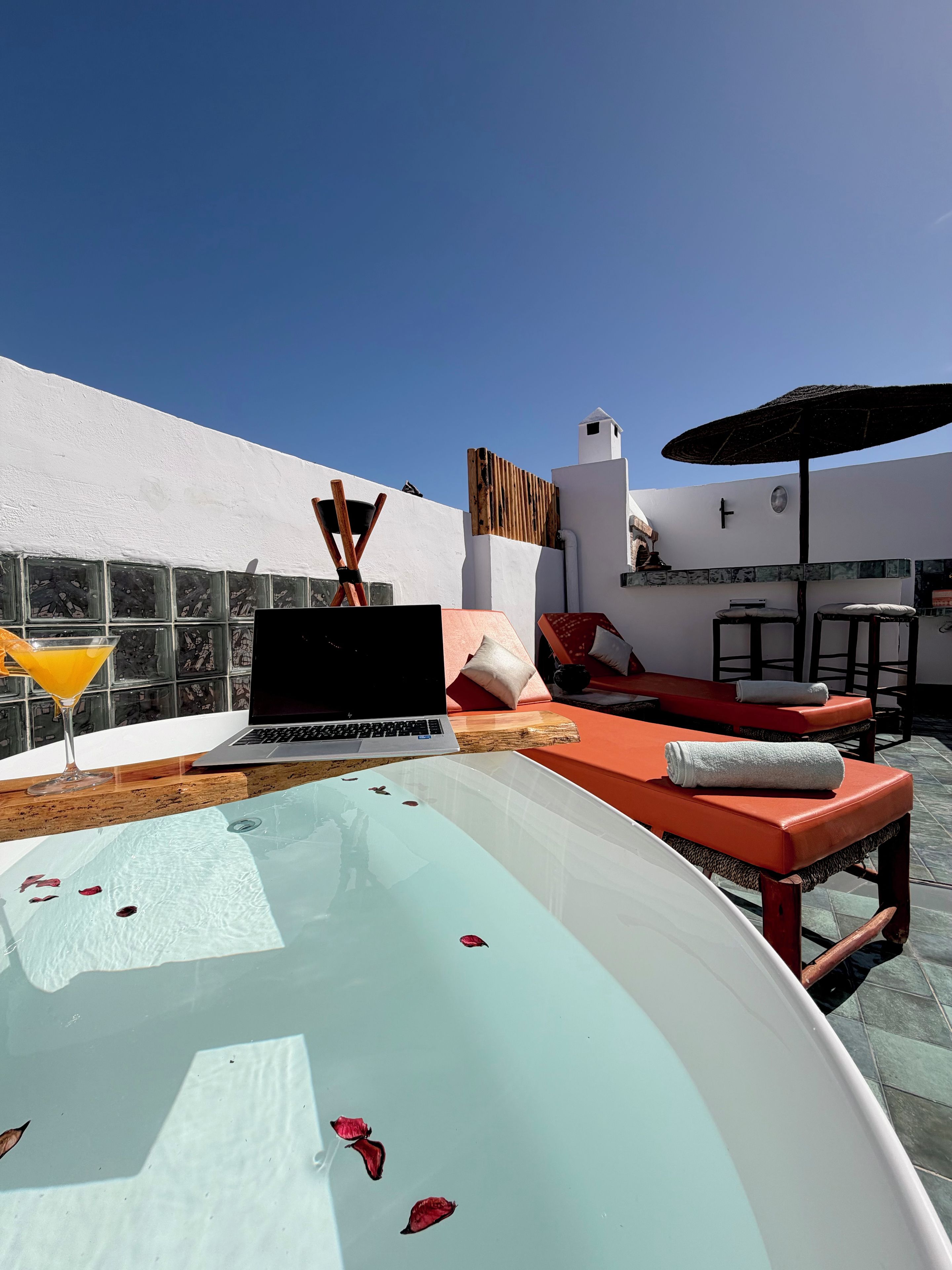 A rooftop pool area with a laptop, lounge chairs, and a drink.