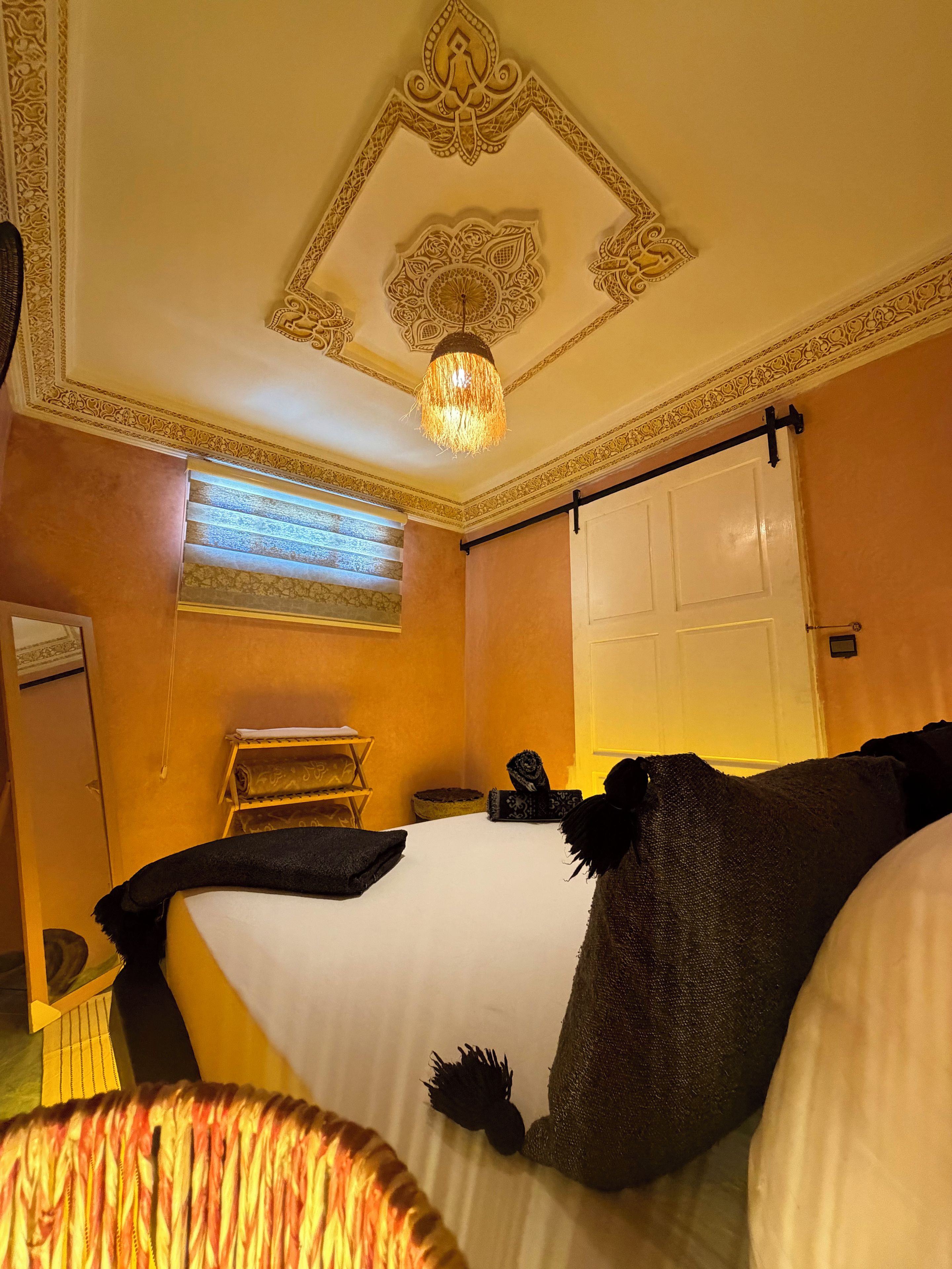 A hotel room with a bed, a window with blinds, a door, and a decorative ceiling.