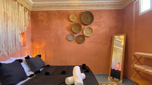 A bedroom with a bed, pillows, a mirror, and a wall with decorative plates. - Uniquely styled apartment with private terrace (Essaouira)