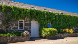 A stone building with a white door and window, covered in green ivy, and a small bush in front. - CRAFNANT -  a cottage that sleeps 4 guests  in 2 bedrooms (Pwllheli)