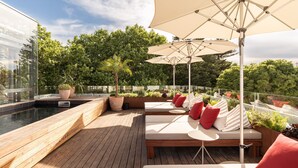 A rooftop terrace with wooden flooring, a pool, and lounge seating with umbrellas.