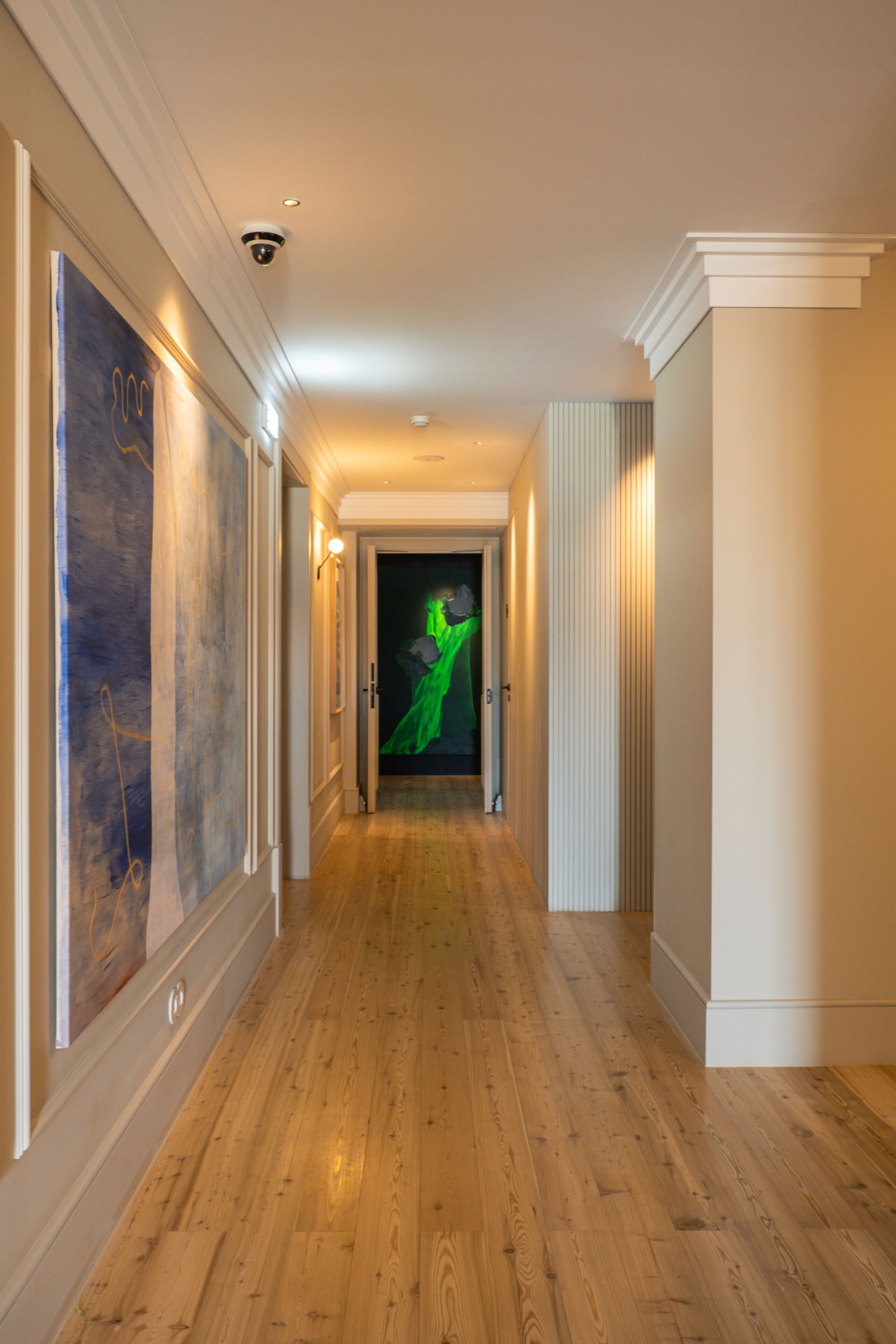 Un couloir avec un plancher en bois, une caméra de surveillance et une porte au fond.
