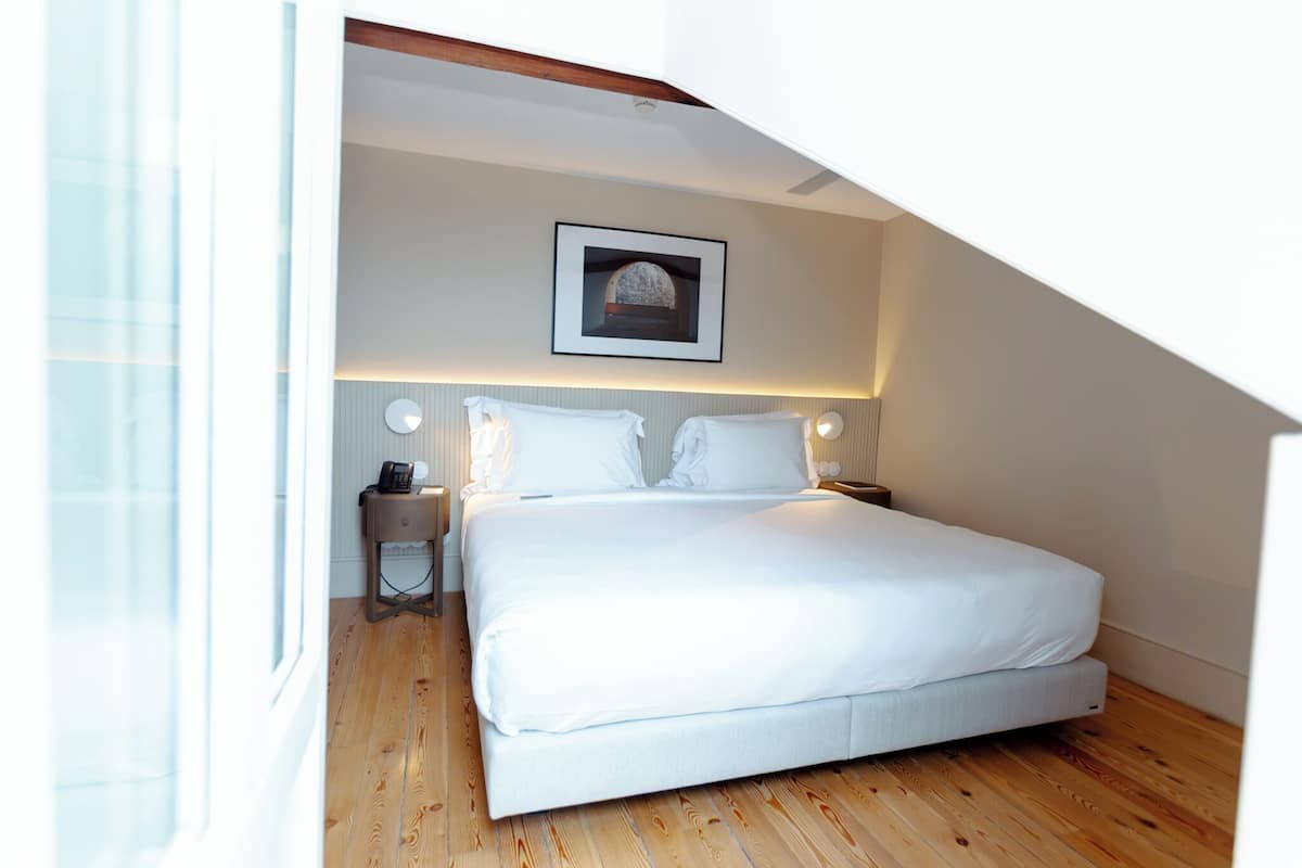 Quarto com cama, mesas de cabeceira, um quadro na parede e uma janela.