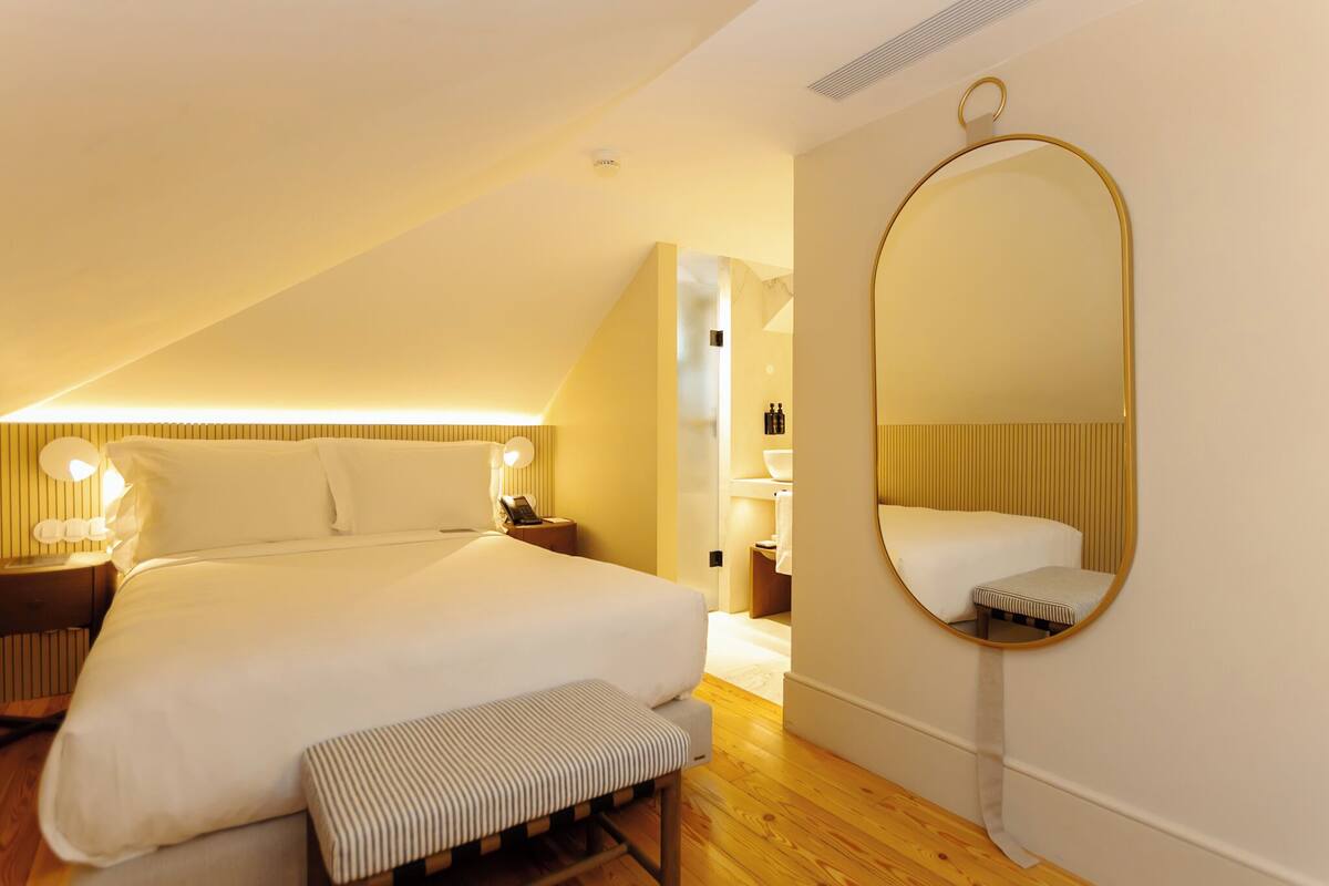 Quarto com cama grande, mesas de cabeceira, espelho e um banco.