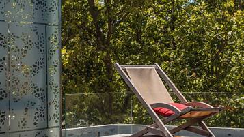 Zona de piscina con una silla de descanso, un separador de vidrio con diseños recortados y un fondo arbolado.