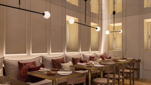 A restaurant with multiple tables, cushioned seating, and pendant lighting.