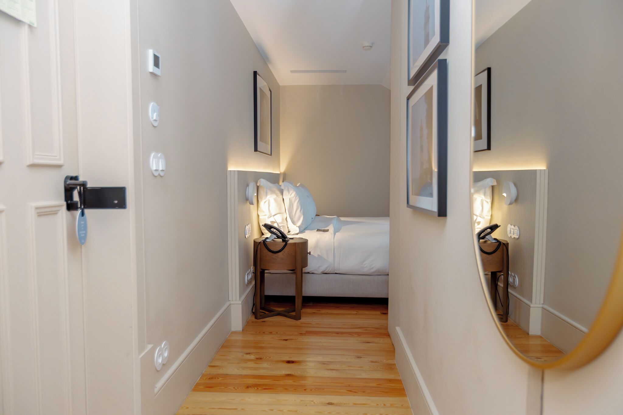 Un pasillo estrecho que conduce a un dormitorio con cama, mesitas de noche y un espejo.