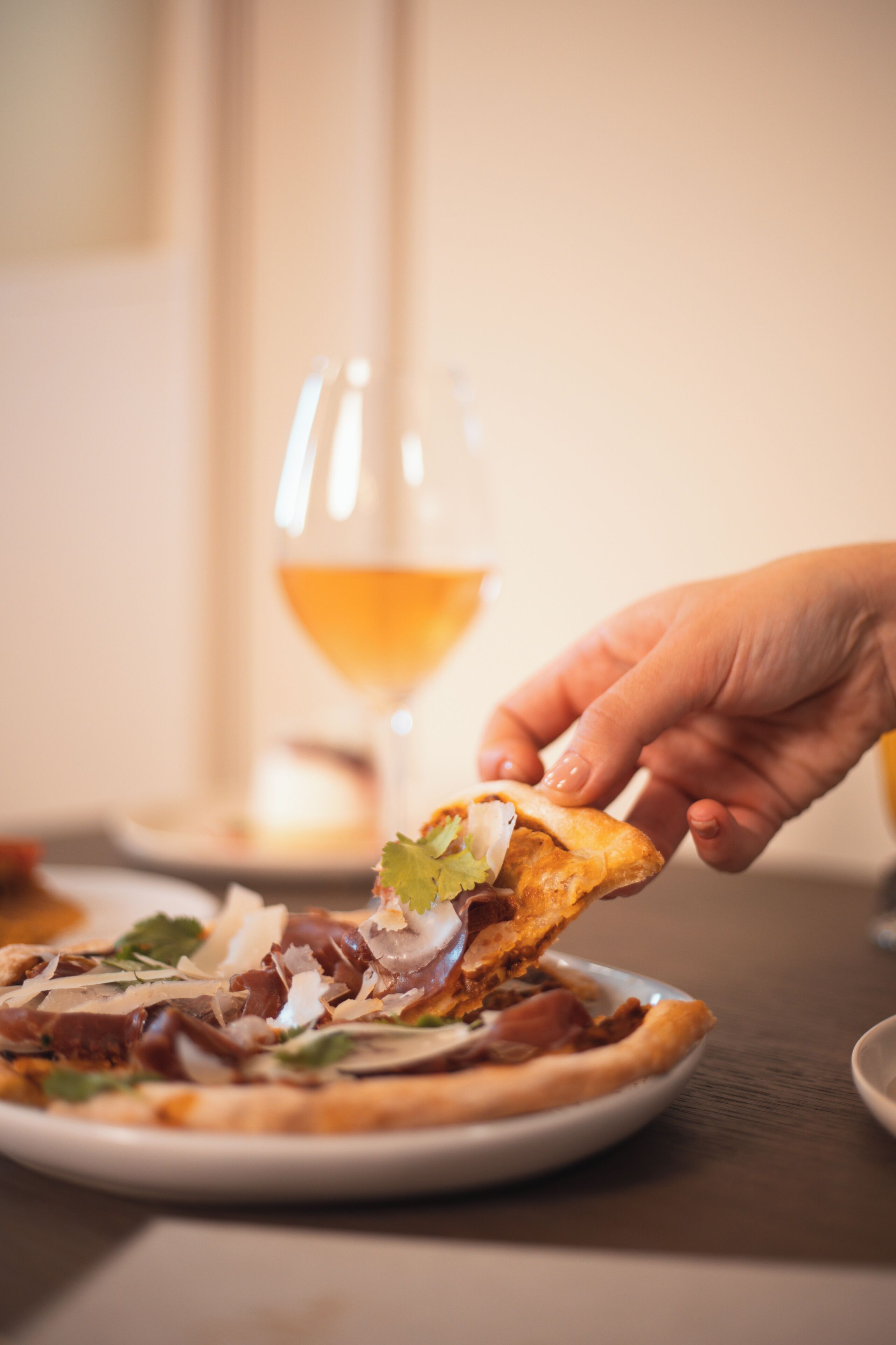 Eine Hand hebt ein Pizzastück von einem Teller.