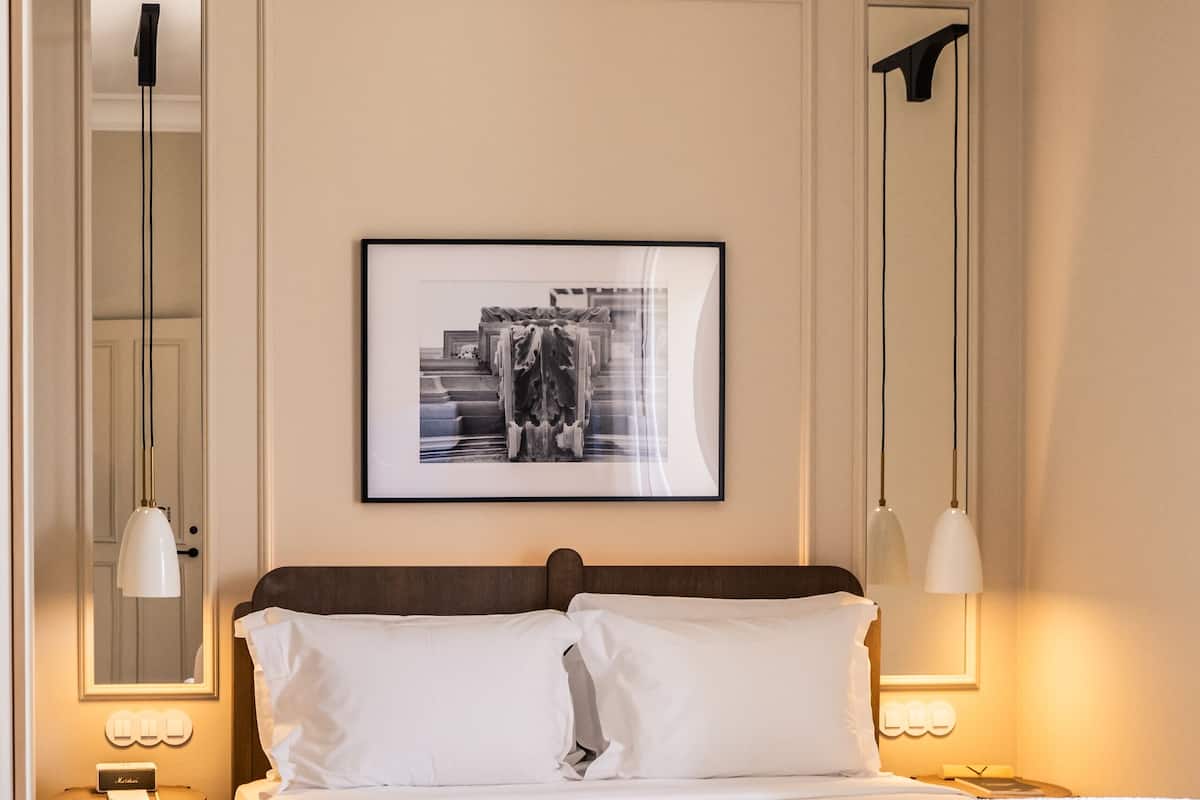 Um quarto bem arrumado com uma cama grande, mesas de cabeceira, um quadro na parede e um espelho.